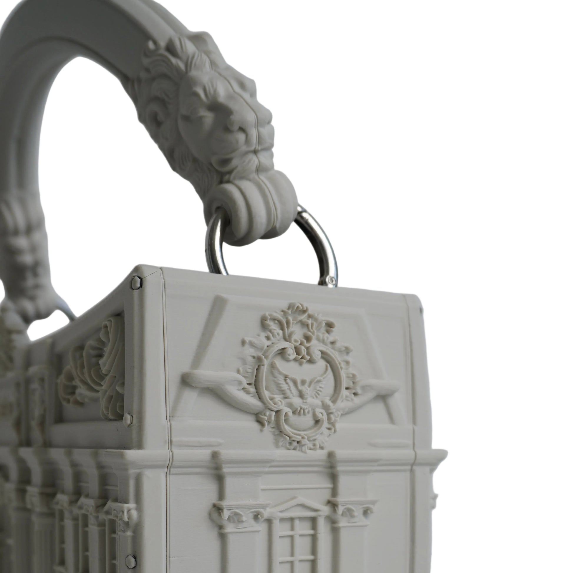 A 3D-printed miniature building-shaped handbag in an off-white color, featuring detailed architectural carvings, a decorative crest on the front, and a sculpted lion head handle with a metal ring.