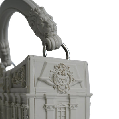 A 3D-printed miniature building-shaped handbag in an off-white color, featuring detailed architectural carvings, a decorative crest on the front, and a sculpted lion head handle with a metal ring.